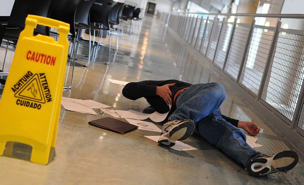 man laying on the ground after falling near wet floor sign