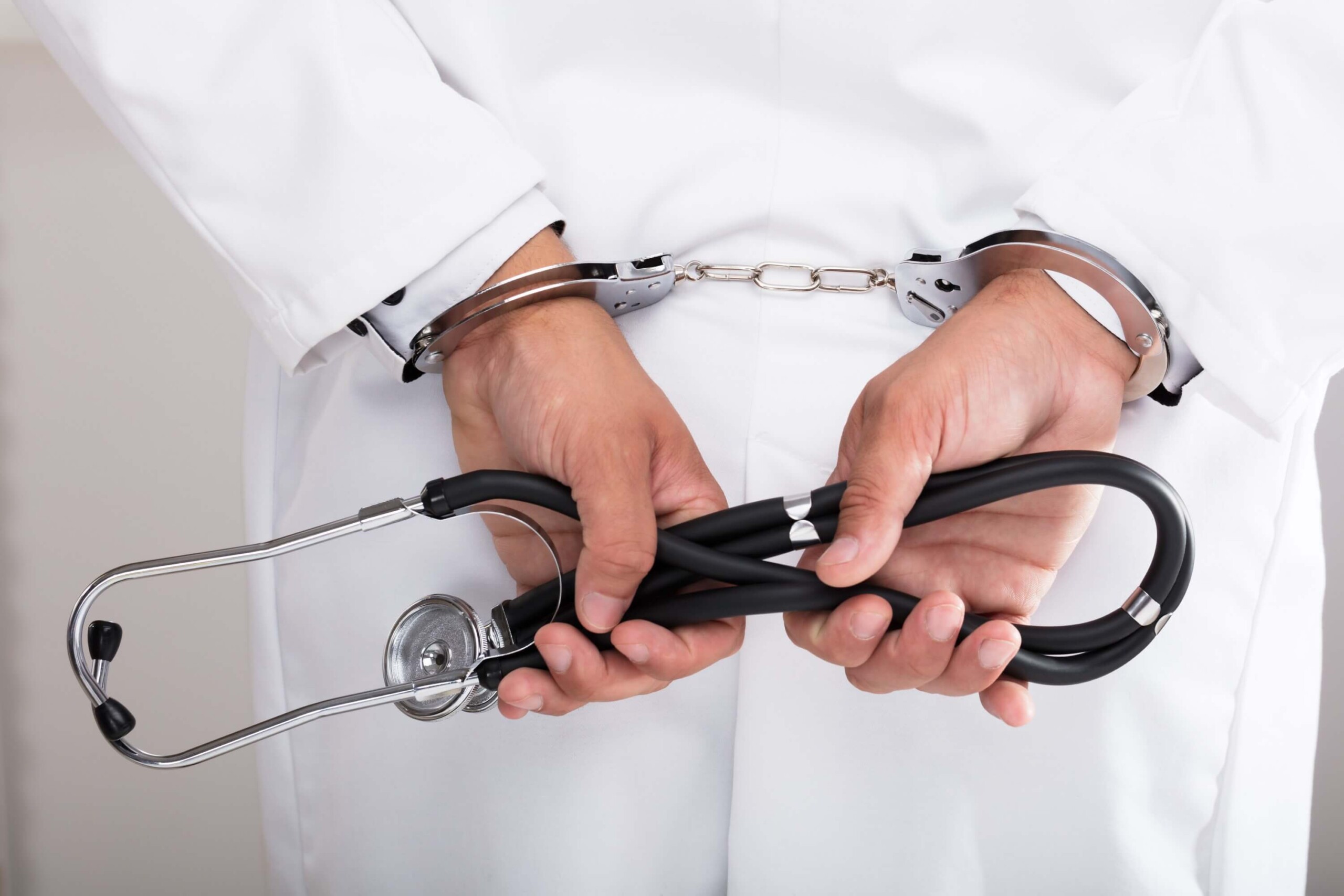 Doctor's hand with handcuffs holding stethoscope behind